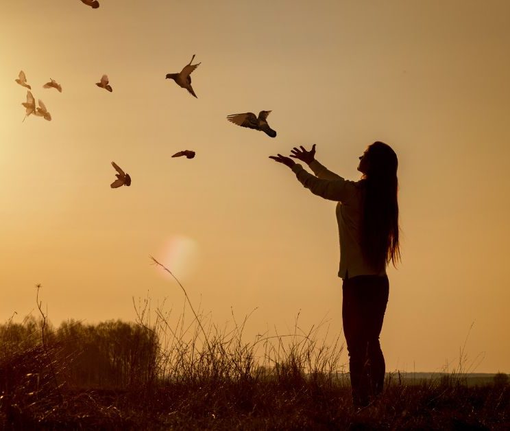 Woman releasing doves into the air at sunset.